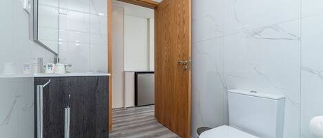 A modern bathroom with a marble wall, a wooden door, a white toilet, and a sink with a mirror.