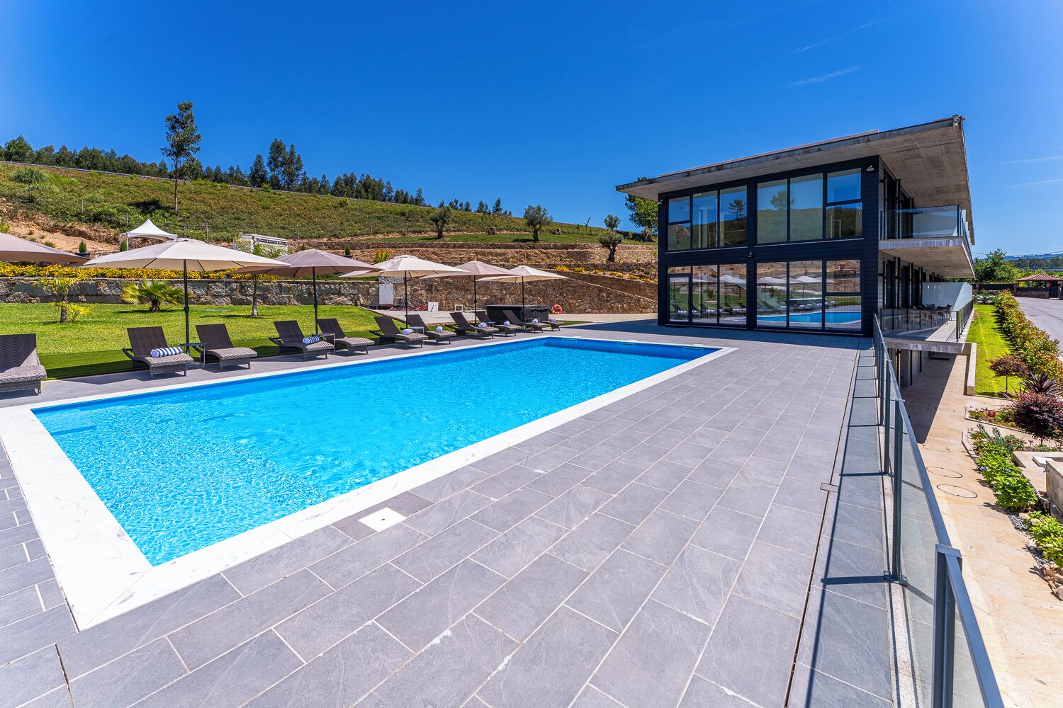 A swimming pool with lounge chairs, a modern building with large windows, and a landscaped garden.
