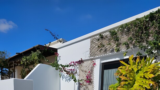 Um edifício branco com uma placa de boas-vindas, uma cadeira preta e um vaso de planta.