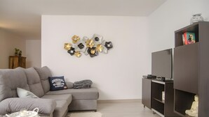 Sala de estar com sofá cinza, um objeto decorativo fixado na parede, um rack de entretenimento escuro e uma pequena estátua.