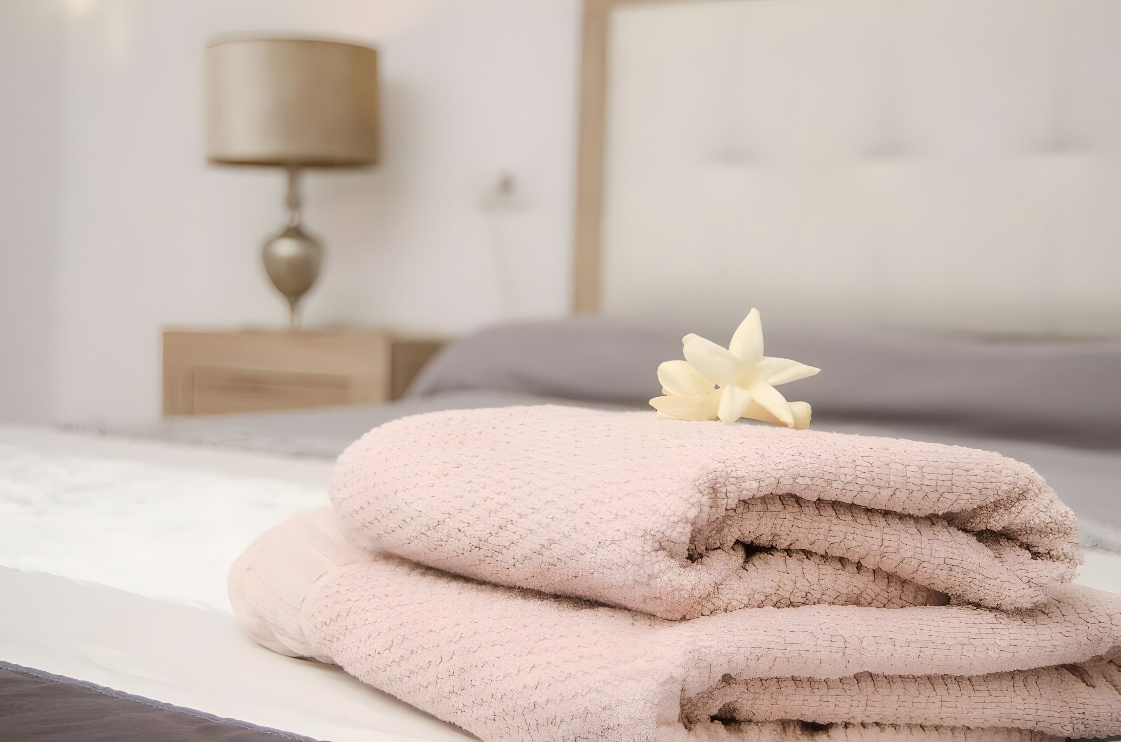 A neatly made bed with folded towels and a decorative flower.