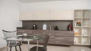 Cozinha moderna com mesa de vidro, duas cadeiras e máquina de café.
