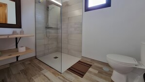 A modern bathroom with a glass-enclosed shower, a toilet, and a small shelf with toiletries. - Alunita Room – Cozy Retreat in Peaceful Nazaret, Lanzarote (Nazaret)