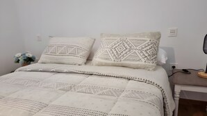 A bed with patterned bedding, a bedside table with a lamp, and a wall socket. - Alunita Room – Cozy Retreat in Peaceful Nazaret, Lanzarote (Nazaret)