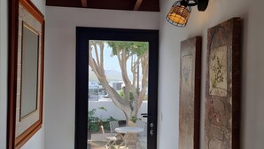 A hallway with a wooden ceiling, a door leading to an outdoor area with a tree and potted plants, and two wall-mounted artworks. - Alunita Room – Cozy Retreat in Peaceful Nazaret, Lanzarote (Nazaret)