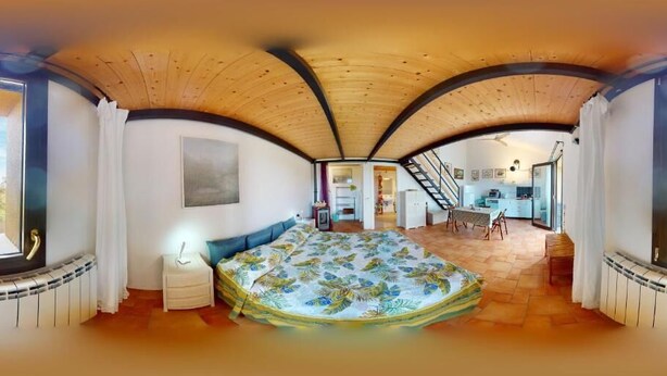 A room with a curved ceiling, a bed with a floral bedspread, a small bedside table, and a window with curtains. - Studio apartments near Baratti Bay (Toscana)