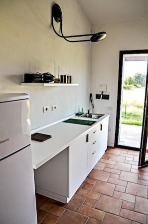 Une cuisine de taille réduite, dotée d’un plan de travail blanc, d’un évier encastré et d’un réfrigérateur.