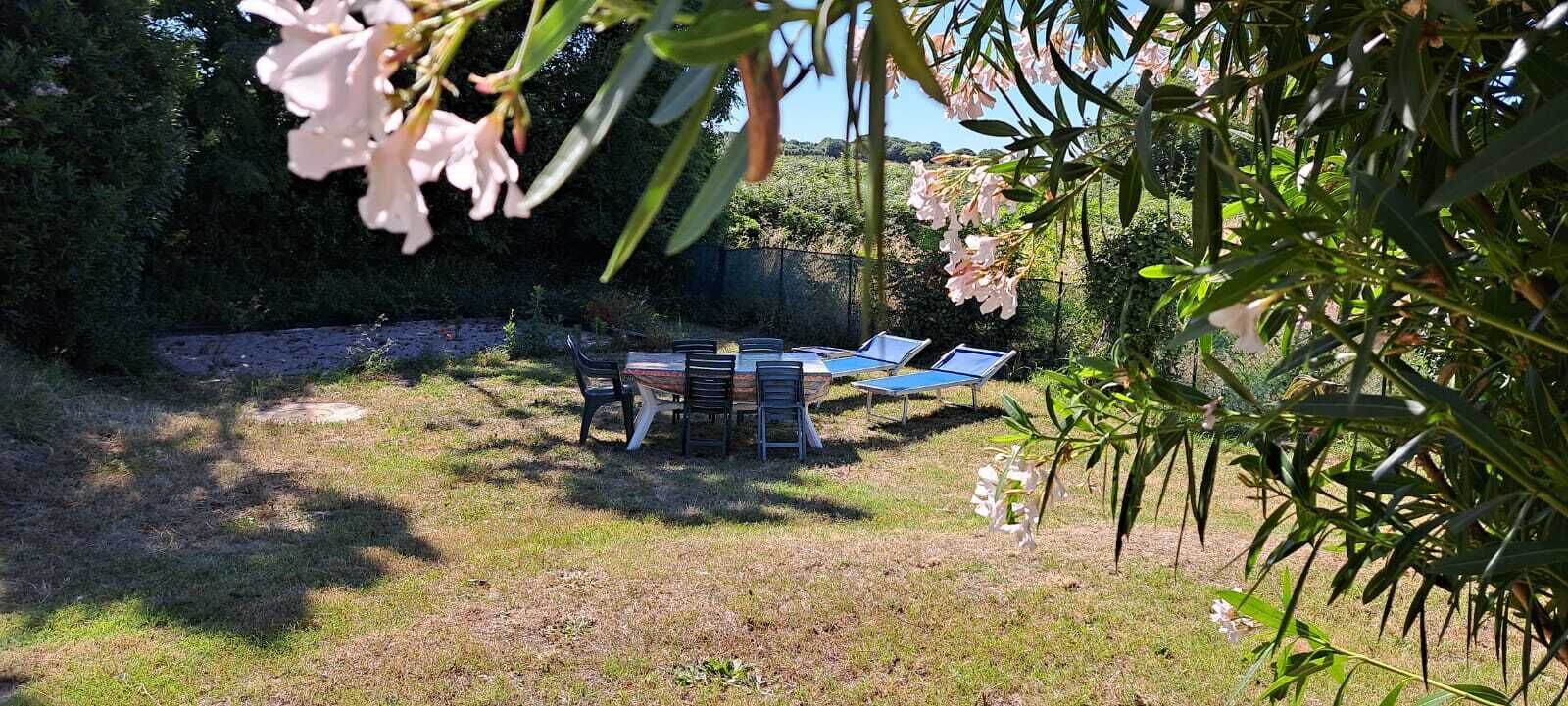 An outdoor seating area with tables and chairs, surrounded by greenery and a stone wall.