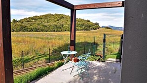 A covered outdoor area with a table and chairs, a view of a grassy field, and a hill in the background. - Studio apartments near Baratti Bay (Toscana)