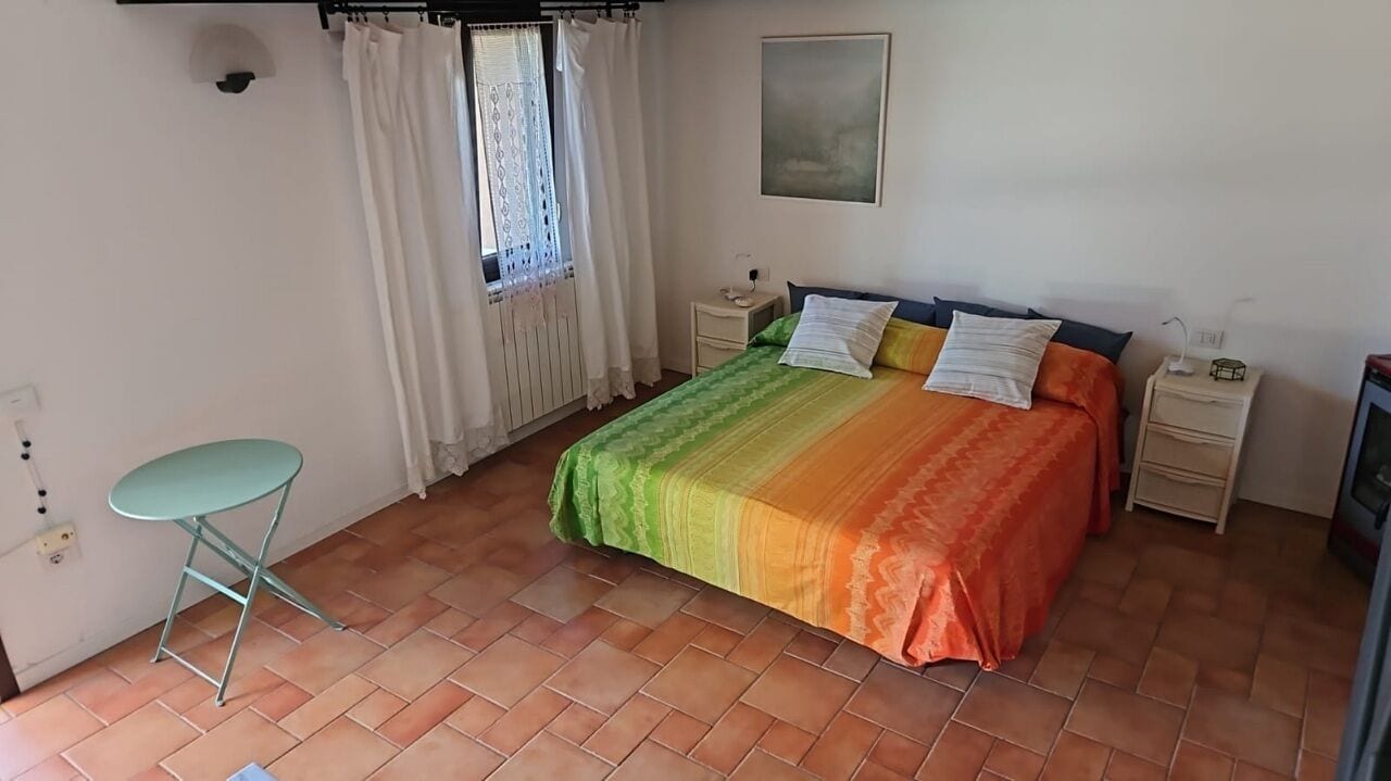 Une chambre à coucher comprenant un lit, une table de chevet, une chaise, une fenêtre avec des rideaux et un tableau accroché au mur.