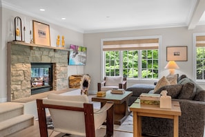 A living room with a stone fireplace, comfortable seating, a television, and large windows with a view of greenery. - Topnotch Luxury Retreat | Sleeps 12 • Pet Friendly • Game Room (Stowe)