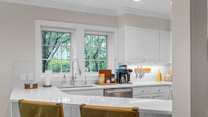 A modern kitchen with white cabinetry, a large island, and a view of greenery outside. - Topnotch Luxury Retreat | Sleeps 12 • Pet Friendly • Game Room (Stowe)