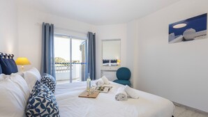 Ein Hotelzimmer mit einem Bett, einem Sessel, einem Tisch mit Flasche und Gläsern, einem Spiegel und Blick durch ein Fenster.