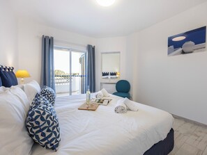 Ein Hotelzimmer mit einem Bett, einem Sessel, einem Tisch mit Flasche und Gläsern, einem Spiegel und Blick durch ein Fenster.