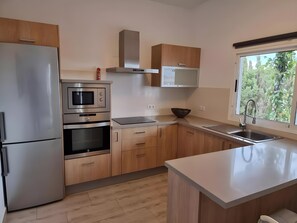 A modern kitchen with stainless steel appliances, wooden cabinets, and a window with a view of greenery.