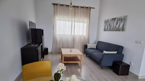 En moderne stue med sofa, fjernsyn, spisebord og sofabord med blomster.