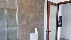 Et moderne badeværelse med et glasbadeværelsesafskærmning, et toilet og en dør til et andet rum.
