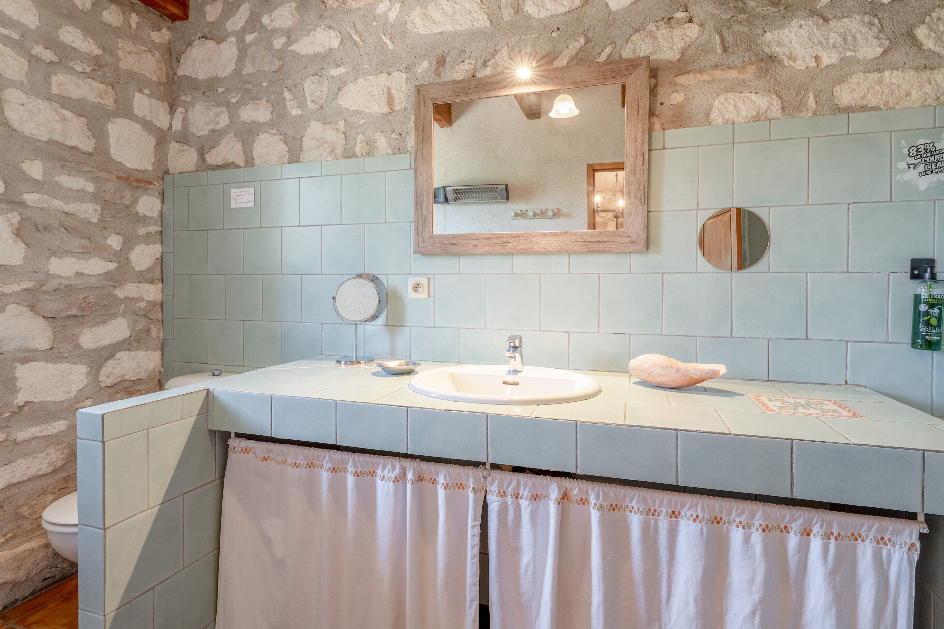 Een badkamer met een stenen muur, een wastafel, een spiegel en een handdoekhouder.