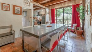 Una cocina rústica con una isla grande, vigas de madera en el techo y vistas a través de una ventana con cortinas rojas.