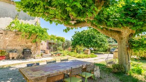 Un espacio de comedor al aire libre con una mesa y sillas de piedra, rodeado de vegetación y un edificio de piedra.