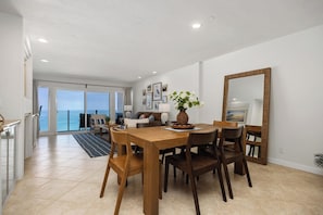 A dining area with a wooden table and chairs, a vase with flowers, and a large mirror on the wall. - Solana Sunshine! Oceanfront Condo in Solana Beach with Tesla Charger (Solana Beach)