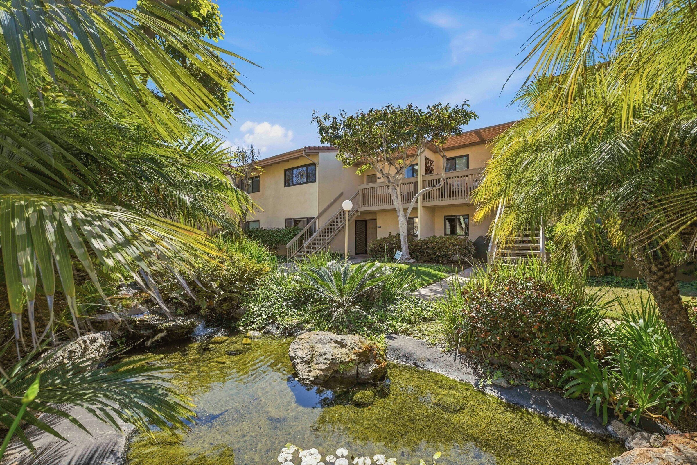 A courtyard with a small pond, palm trees, and a building with balconies.