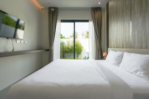 A hotel room with a large bed, a TV mounted on the wall, and a view of greenery outside. - Brand new 3BR Pool Villa with Outdoor Dining (Si Sunthon)