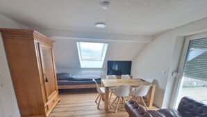 A compact room with a loft bed, a dining table with chairs, a leather sofa, and a large window. - Cozy guest rooms in a modern, renovated apartment (Schwäbisch Gmünd)