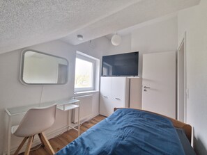 Un dormitorio con cama, escritorio, silla, televisor y armario.