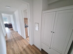 Ein Flur mit Holzboden, einem weißen Kleiderschrank und einer sichtbaren Steckdose.