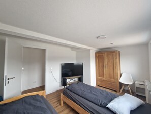 Ein Zimmer mit einem Bett, einem Fernseher, einem Kleiderschrank und einem Schreibtisch mit einer Lampe.