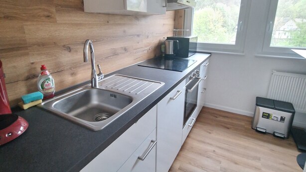 A modern kitchen with a wooden floor, white cabinets, a stainless steel sink, and a window providing natural light. - Cozy guest rooms in a modern, renovated apartment (Schwäbisch Gmünd)