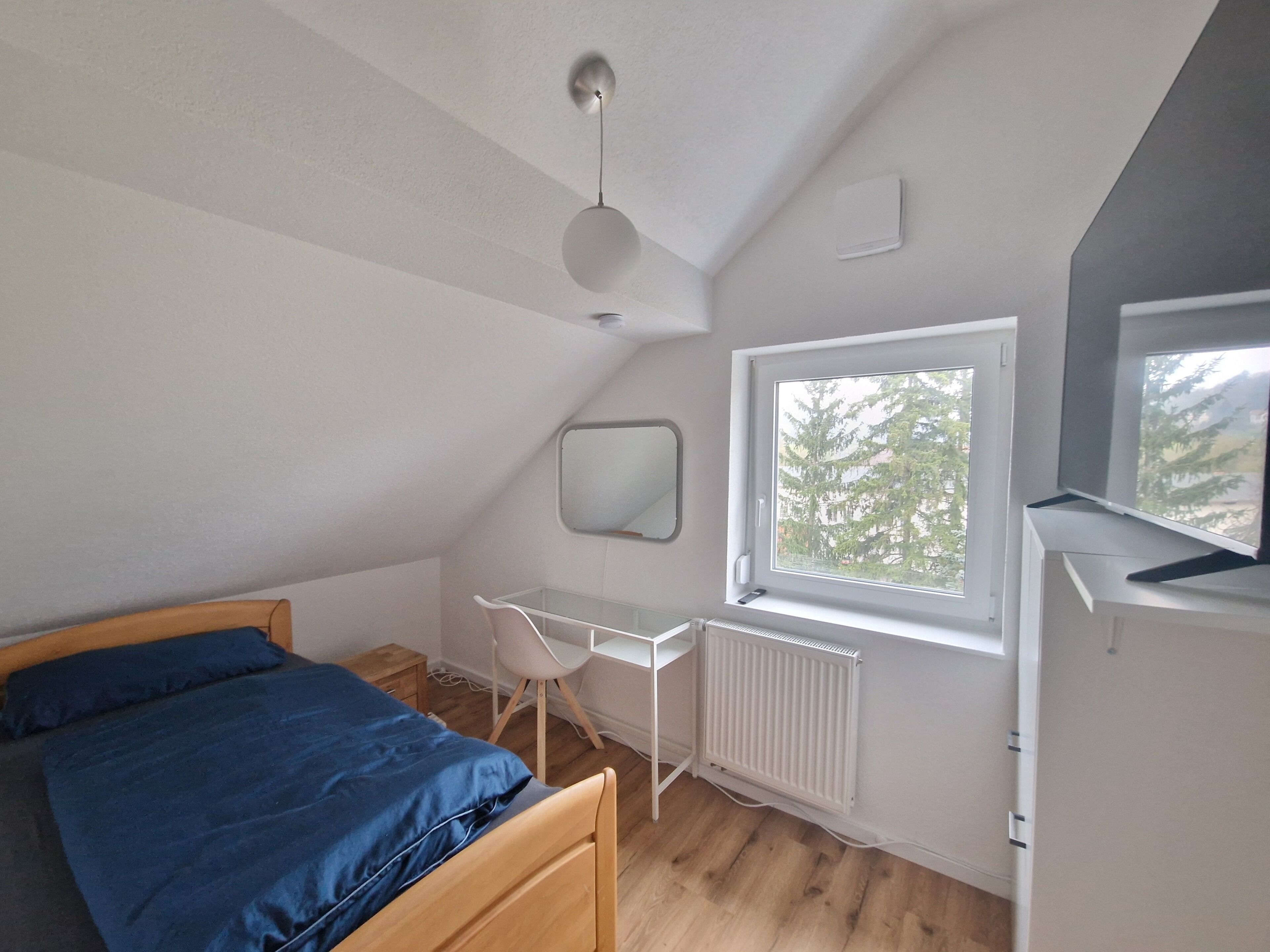 Een slaapkamer met een bed, een bureau, een stoel, een radiator en een raam.