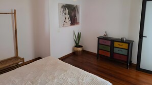 Una camera da letto con un letto, un lampadario a sospensione, un quadro appeso al muro, una pianta in vaso, una panca di legno e una cassettiera multi cassetto.