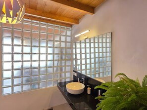 A bathroom with a large window, a round sink, a mirror, and a ceiling light fixture.