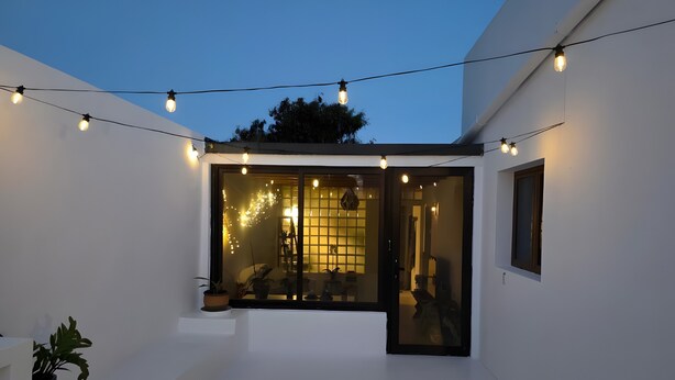 Una casa moderna con ingresso tramite porta in vetro, un piccolo spazio esterno con piante in vaso e luci decorative.
