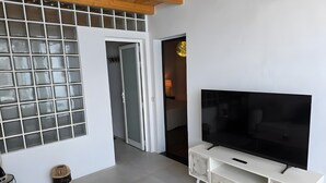 Un soggiorno con televisore, un tavolino in legno, una poltrona in vimini e un mobile porta TV bianco.