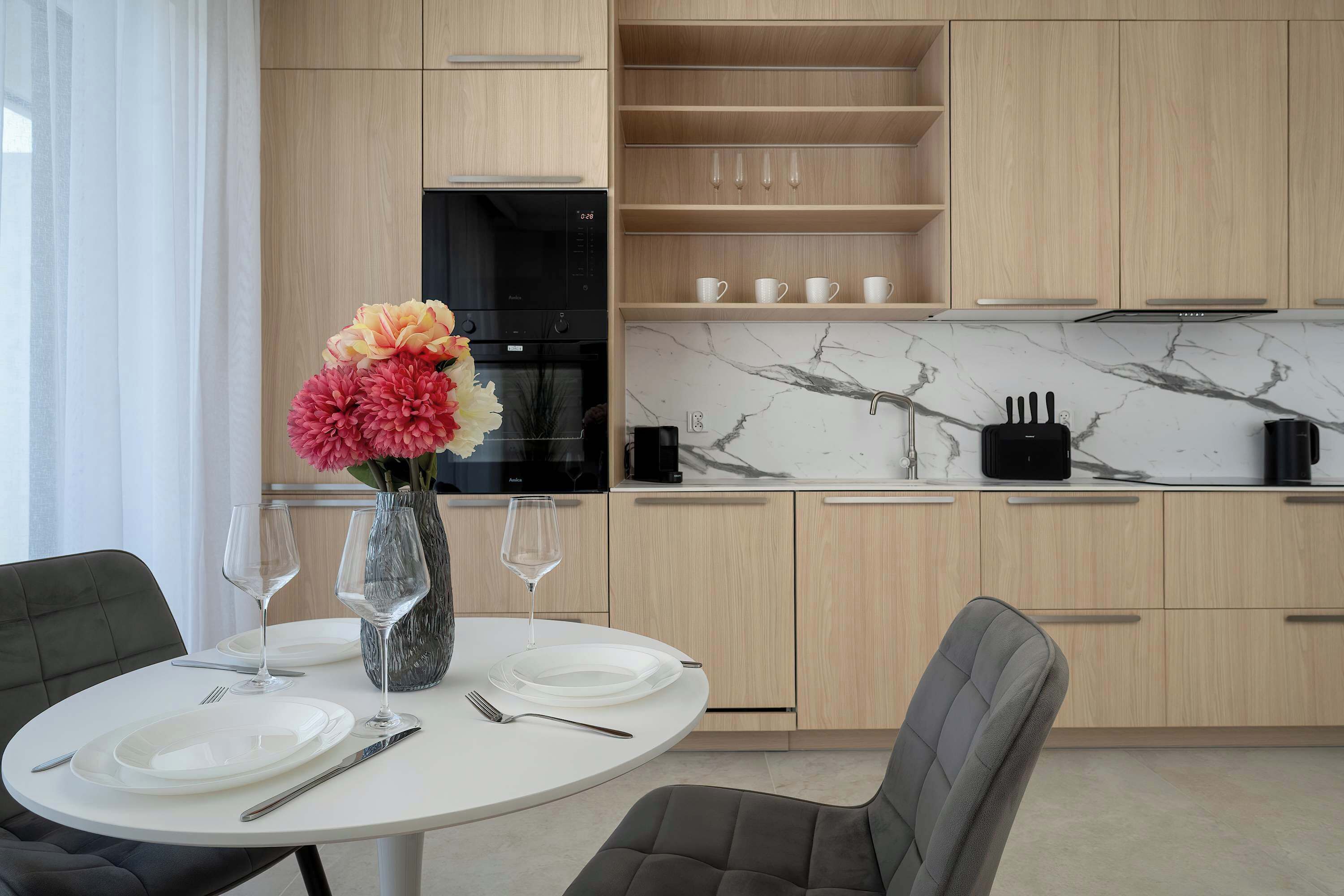 A modern kitchen with a marble countertop, wooden cabinets, and a dining area with a round table set for two.