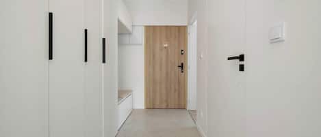 A hallway with white walls, a wooden door at the end, and a light switch on the wall.