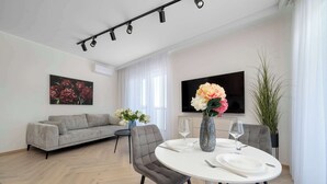 Una sala moderna con un sofá gris, una mesa de comedor redonda con platos blancos y un jarrón con flores.