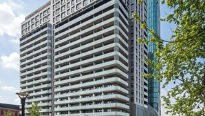 Un edificio de varios pisos con un diseño arquitectónico moderno, que combina balcones y ventanas, rodeado de vegetación y un cielo despejado.