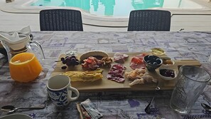 A breakfast table with a variety of foods, a glass of orange juice, and a view of a pool.