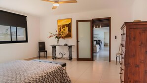 A bedroom with a bed, a desk, a chair, a wooden cabinet, a painting, and a sliding door leading to a bathroom.