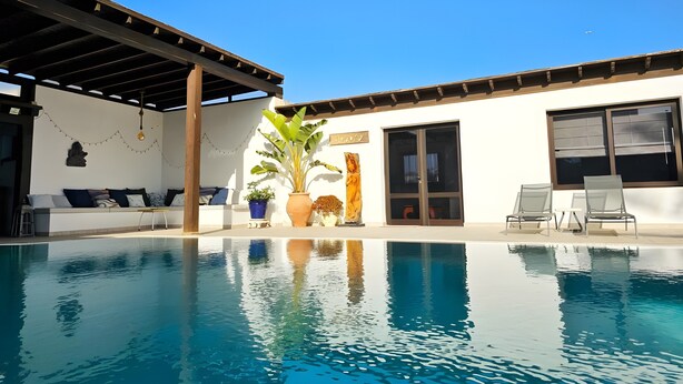 A pool area with a covered seating area, a potted plant, and a statue.