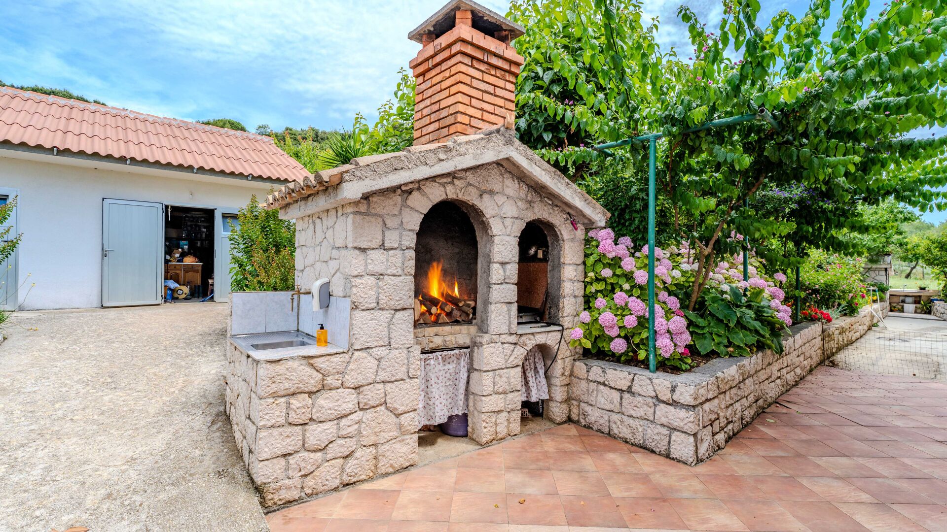 A stone-built outdoor kitchen with a chimney, a sink, and a fire pit.