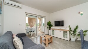 A modern living room with a sofa, a small wooden table, a TV, and a sliding glass door leading to an outdoor area. - Apartman Sunset View Rab by Villas Guide (Rab)