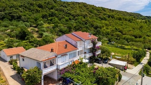 A two-story building with a red-tiled roof, surrounded by lush greenery and a hillside. - Apartman Sunset View Rab by Villas Guide (Rab)