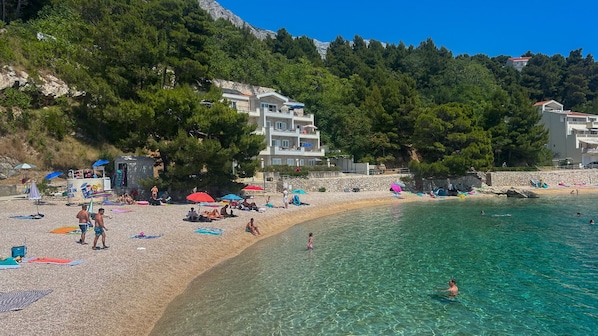 A beach with clear water, people sunbathing, and buildings in the background.