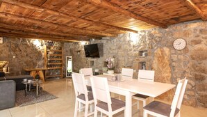 A stone-walled room with a wooden ceiling, a dining table with chairs, a television, and a fireplace. - Holiday Home Stari Dom Ivkošic by Villas Guide (Zmijavci)