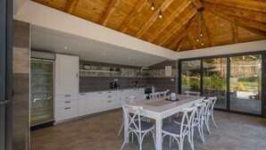 A modern kitchen with white cabinetry, a large island with seating, and a view through glass doors to an outdoor area. - Holiday Home Stari Dom Ivkošic by Villas Guide (Zmijavci)